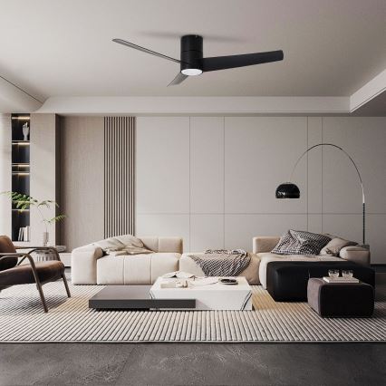 Čierny stropný ventilátor s tromi lopatkami sa otáča v moderne zariadenej obývacej izbe s bielym gaučom, konferenčným stolíkom a kobercom.