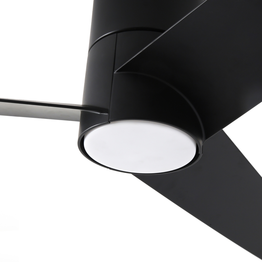 Čierny stropný ventilátor s tromi lopatkami sa nachádza pred bielym difúzorom svetla. Lopatky sú dlhé a úzke, pripevnené k valcovitému čiernemu telu ventilátora.