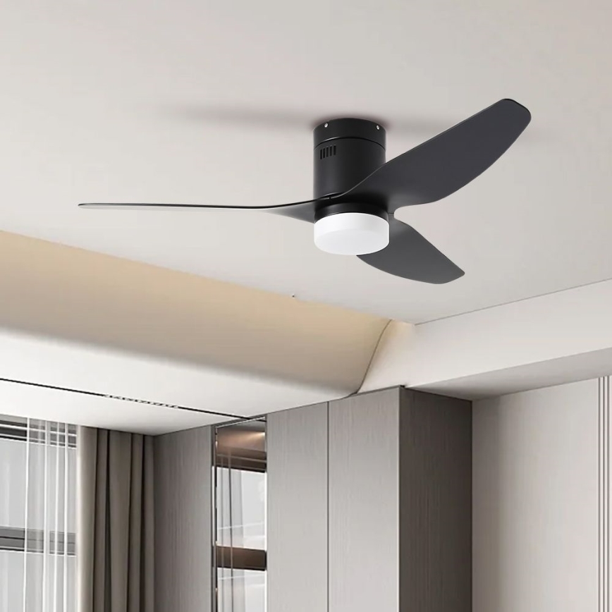 Čierny stropný ventilátor s tromi lopatkami a integrovaným svetlom je pripevnený na strope. Ventilátor je v interiéri miestnosti s nábytkom a závesmi.