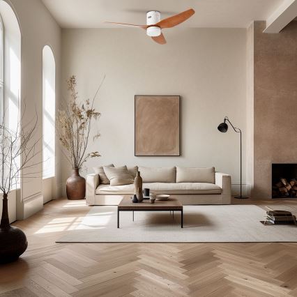 Stropný ventilátor s drevenými lopatkami rotuje v svetlej obývacej izbe s béžovou sedačkou, nízkym konferenčným stolíkom a parketovou podlahou. V miestnosti sú tiež váza s konárikmi, obraz a stojacia lampa.