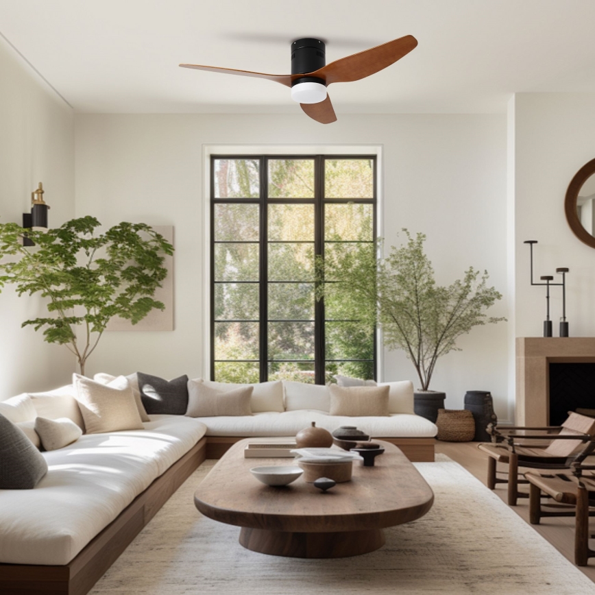 Stropný ventilátor s drevenými lopatkami a čiernym telom sa otáča v svetlej obývacej izbe s bielym gaučom, dreveným konferenčným stolíkom a dvoma izbovými rastlinami.