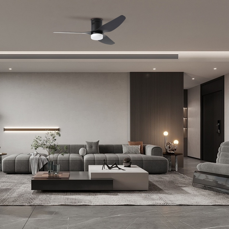 Stropný ventilátor s troma lopatkami sa otáča v modernom obývacej izbe. Izba obsahuje šedú sedačku, konferenčný stolík a koberec.