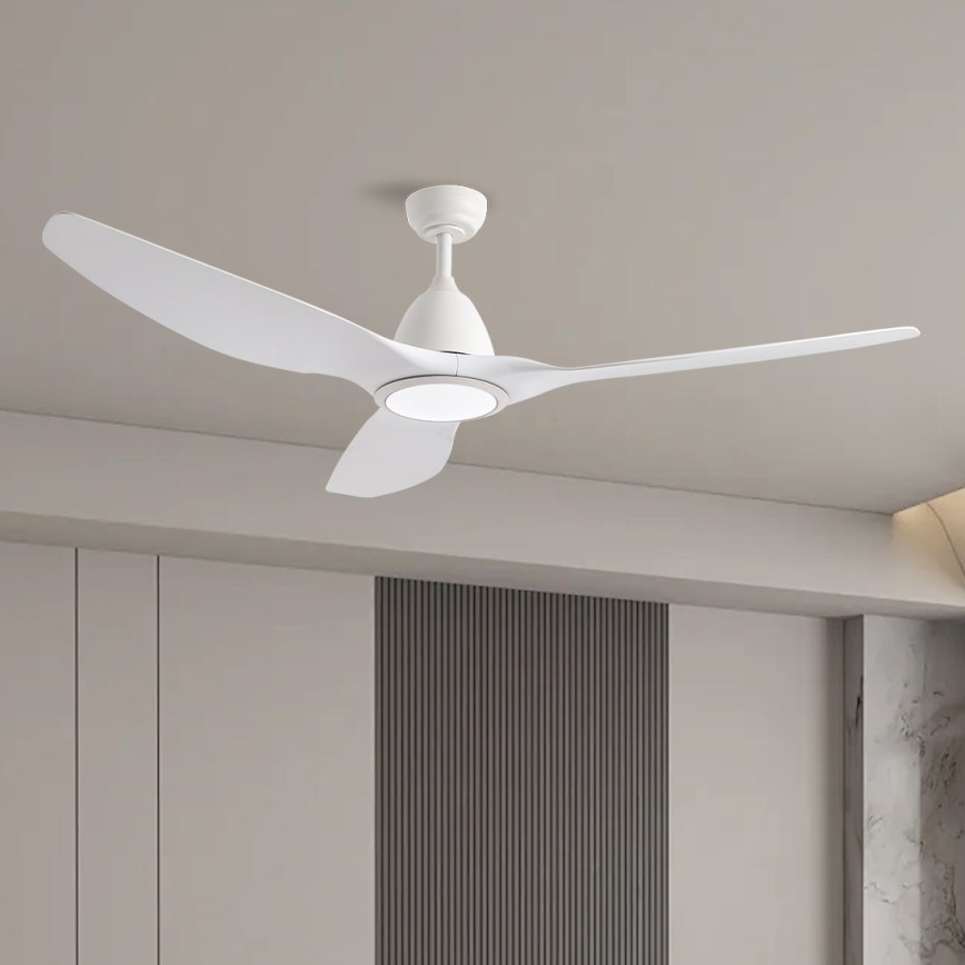 Biely stropný ventilátor s tromi lopatkami sa otáča v interiéri. Ventilátor má zabudované LED svetlo. Nachádza sa v miestnosti s bledými stenami a vertikálnymi tmavými panelmi.