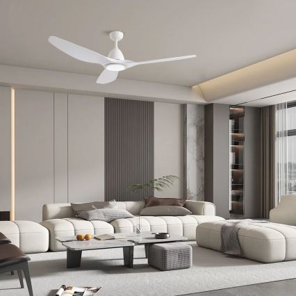 Biely stropný ventilátor s tromi lopatkami sa otáča v moderne zariadenej obývacej izbe s bielou sedačkou, nízkym konferenčným stolíkom a doplnkovým nábytkom.