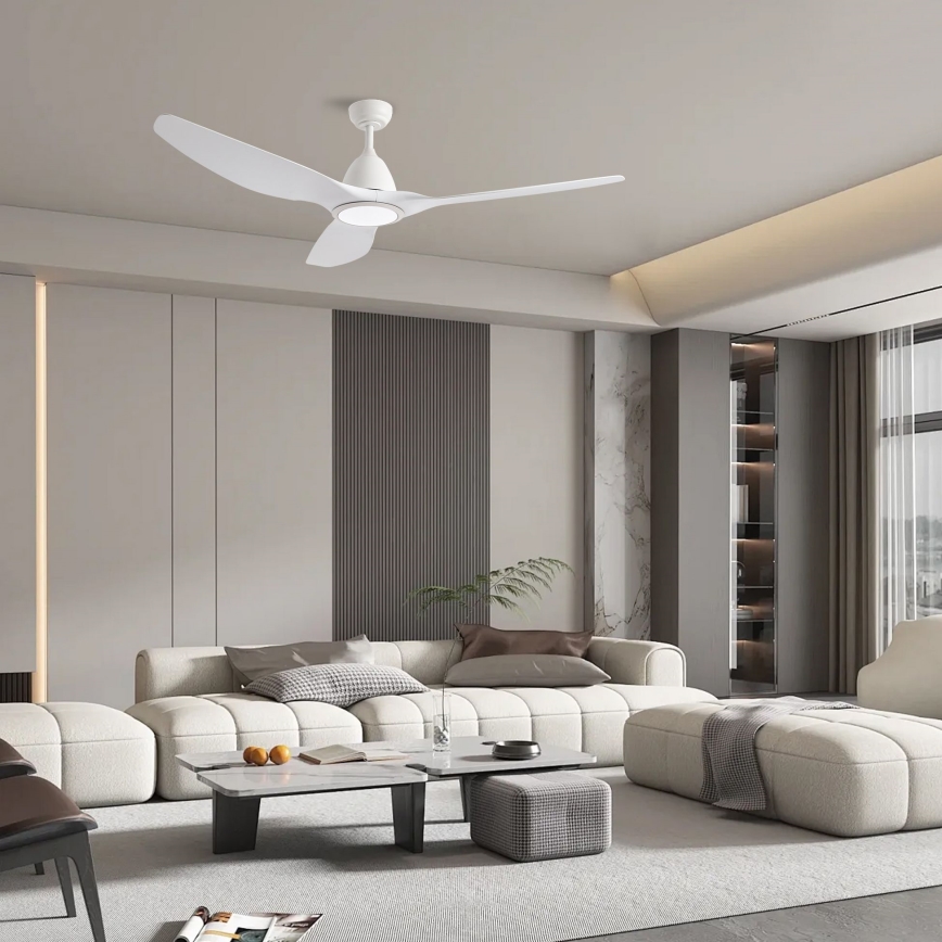 Biely stropný ventilátor s tromi lopatkami sa otáča v moderne zariadenej obývacej izbe s bielou sedačkou, nízkym konferenčným stolíkom a doplnkovým nábytkom.