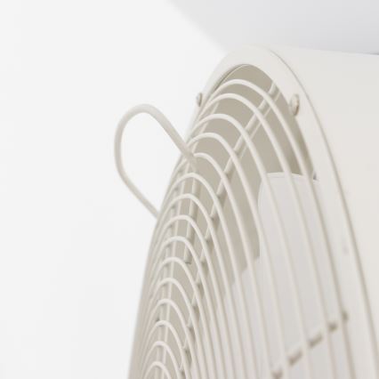 Biely ventilátor s ochrannou mriežkou je pripevnený k stene. Ventilátor má malú, ohnutú kovové držadlo.
