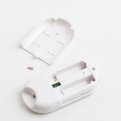 Biely diaľkový ovládač je rozobratý, odhalený priestor pre batérie. Chýba vrchný kryt, viditeľný je šrób. Všetko leží na bielom povrchu.