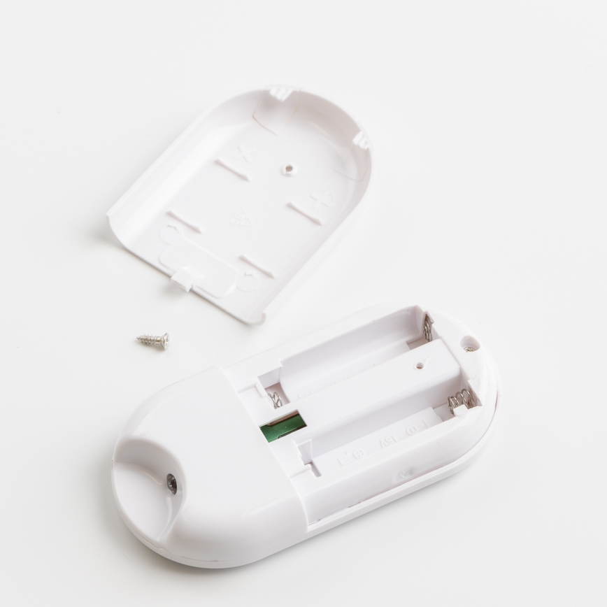 Biely diaľkový ovládač je rozobratý, odhalený priestor pre batérie. Chýba vrchný kryt, viditeľný je šrób. Všetko leží na bielom povrchu.