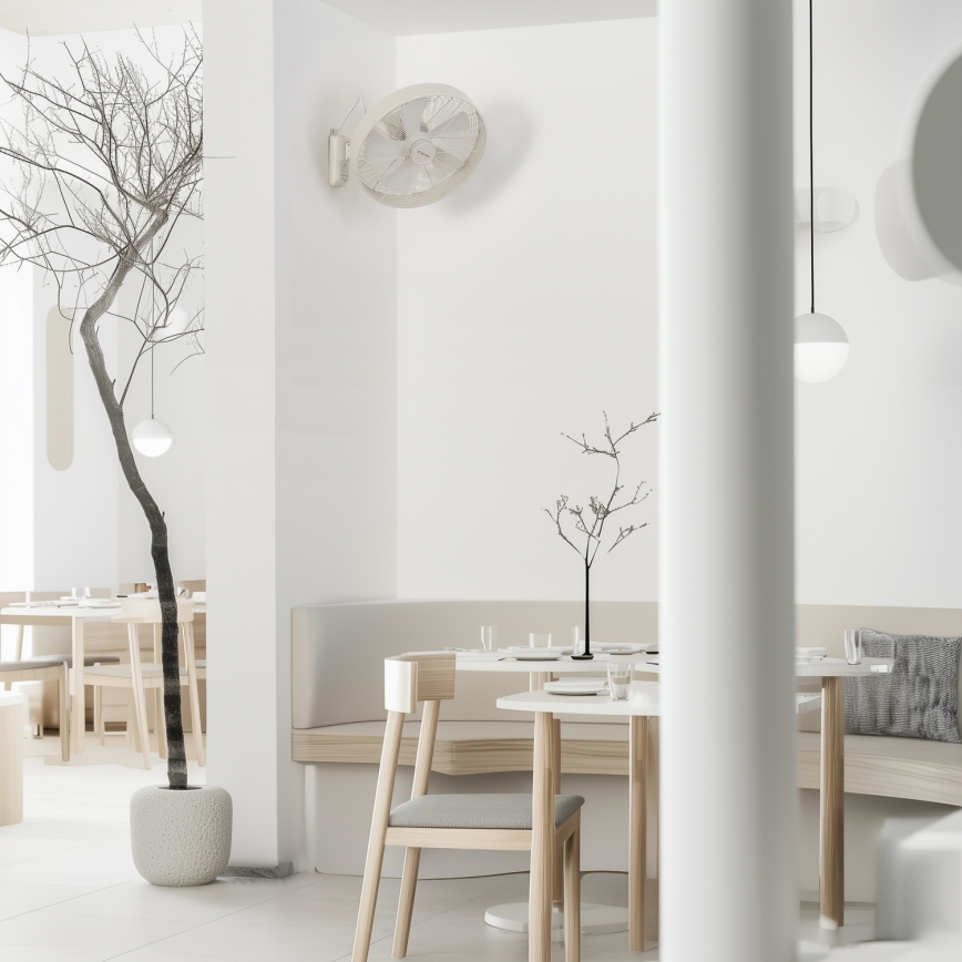 Stôl s dvoma stoličkami sa nachádza v minimalisticky zariadenej reštaurácii s bielymi stenami, dreveným nábytkom a suchými vetvičkami vo váze. Na stene je pripevnený biely ventilátor.