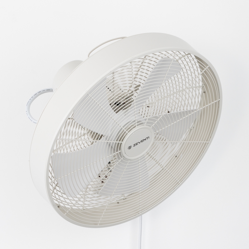 Biely nástenný ventilátor s troma lopatkami rotuje. Je pripevnený na stene, viditeľný je biely kábel. Na ventilátore je logo „ZEVENTI“.