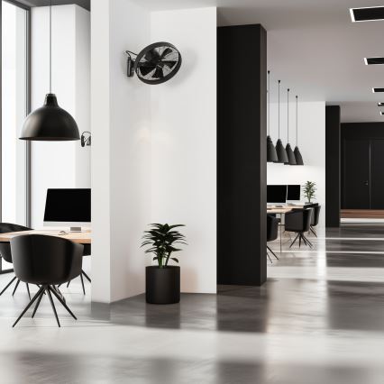 Stropný ventilátor je namontovaný na stene modernej kancelárie. Ventilátor je čierny, kancelária je zariadená v čiernej a bielej farbe, s drevenými prvkami a rastlinou v kvetináči.