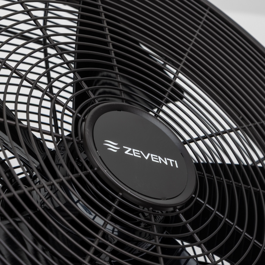 Čierny stolový ventilátor značky ZEVENTI s kovovou ochrannou mriežkou stojí na bielom podklade. Ventilátor je statický. Na stredovej krytke je logo ZEVENTI.