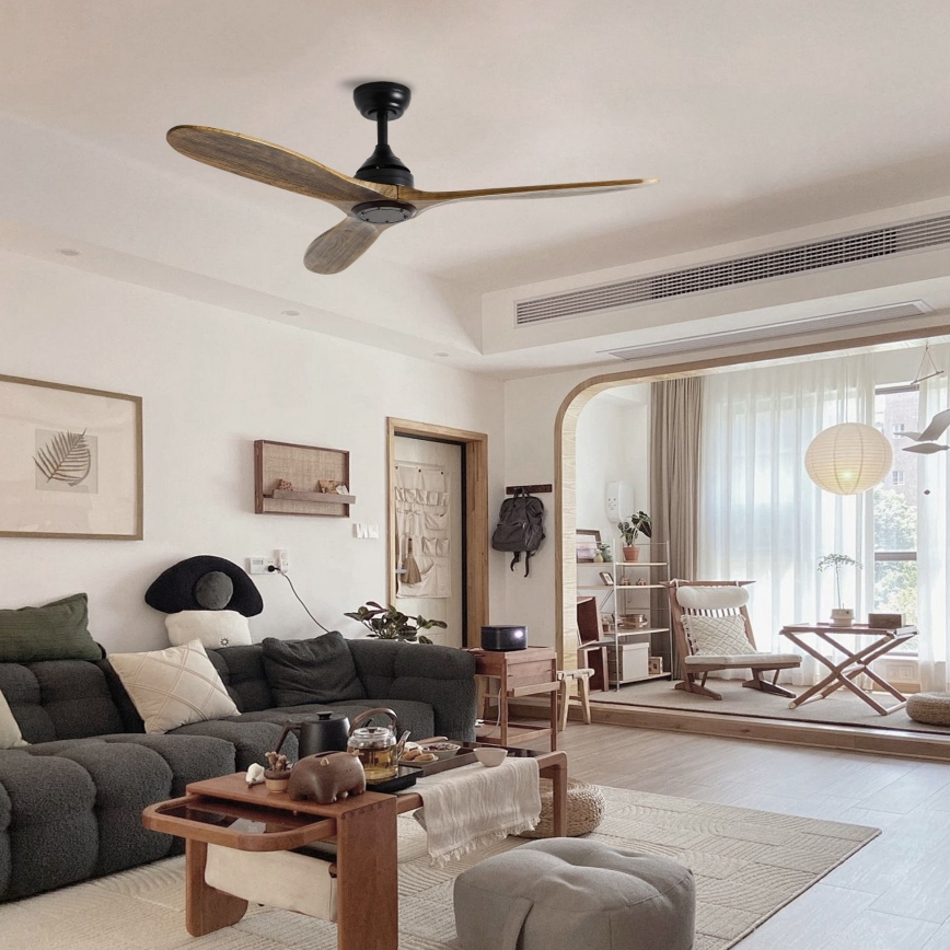 Drevený stropný ventilátor s troma lopatkami rotuje v obývacej izbe zariadenej v minimalistickom štýle s pohovkou, konferenčným stolíkom a doplnkami. Izba má svetlé steny a veľké okná.