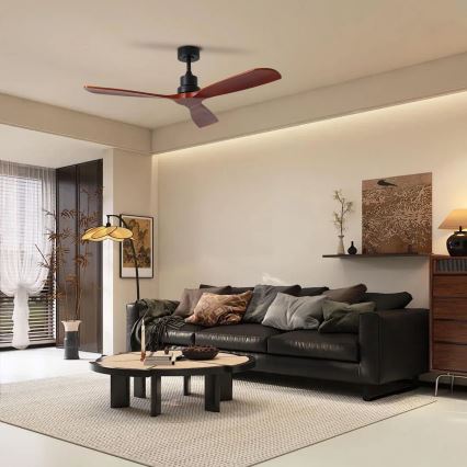 Drevený stropný ventilátor s troma hnedými lopatkami a čiernym motorom sa otáča v moderne zariadenej obývačke s koženou sedačkou a nízkym konferenčným stolíkom. Obývačka obsahuje svetlé steny, koberec a dekorácie.