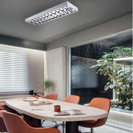 Dlhá, úzka svietidlo svieti v modernej zasadacej miestnosti. Miestnosť obsahuje oválny stôl s oranžovými stoličkami a okná s žalúziami. V pozadí je vidieť zeleň.